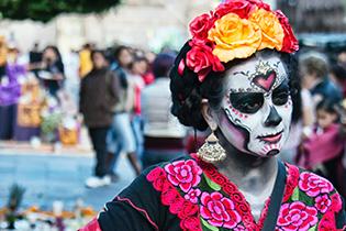 A person wearing day of the dead sugar skull make-up, a flower headband, and traditional spanish dress.