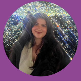 student with white shirt and black jacket standing in front of twinkle lights