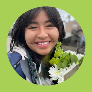 Student with graduation grown holding white and green flowers