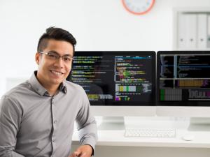 Male student is sitting at a computer with two large monitor